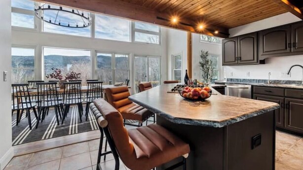 A modern kitchen with a large island, dark cabinetry, and a view of the outdoors. - White Mtn Lux Retreat - Hot Tub, Sauna & Game Room (Bartlett)
