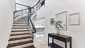 Eine Treppe mit dunklen Holzstufen und schwarzen Metallgeländern, die zu einem Essbereich mit einer Chandelüstere führt.