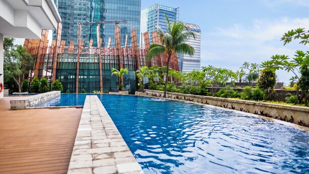 Piscina com deck de madeira e vista para edifícios modernos ao fundo.