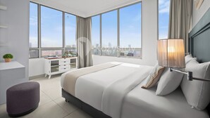 Quarto de hotel moderno com uma cama grande, uma escrivaninha e vista da cidade através de amplas janelas.