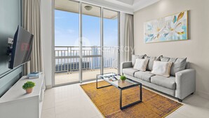 Uma sala de estar moderna com um sofá cinzento, uma mesa de centro de vidro, uma televisão de tela plana e uma janela grande com vista para a cidade.