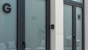 A hotel entrance with a glass door, a reception desk, and a seating area visible through the glass. - VLC HOST - Sumsi G (Valencia)
