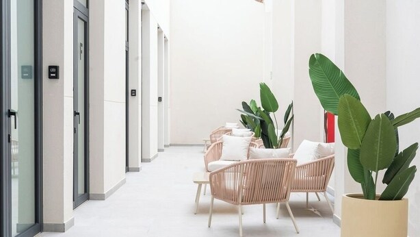 A corridor with wicker chairs and potted plants, leading to a door with a sign. - VLC HOST - Sumsi G (Valencia)