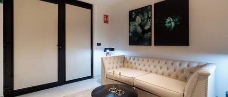 Un soggiorno con un divano color beige, un tavolino nero tondo e due stampe botaniche incorniciate alle pareti.