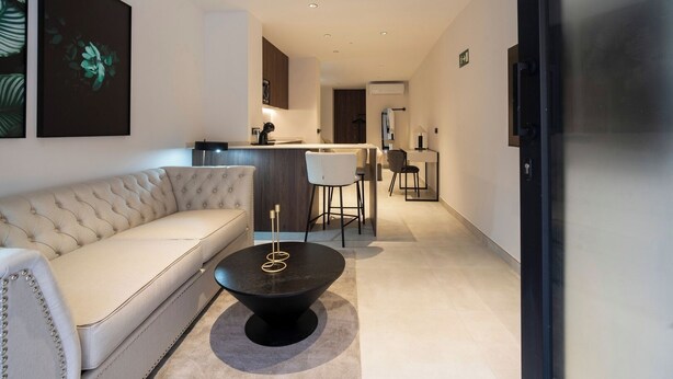 Un salon moderne avec un canapé, une table basse et un coin cuisine à l’arrière-plan.