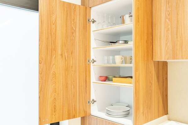 Un meuble en bois doté de plusieurs étagères, contenant des ustensiles de cuisine et de la vaisselle.