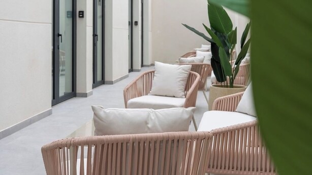 A corridor with wicker chairs and white cushions, a potted plant, and a glass door. - VLC HOST - Sumsi I (Valencia)