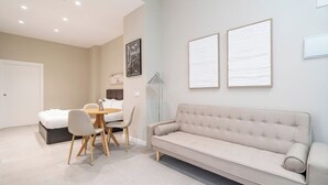 Ein modernes Schlafzimmer mit einem Bett, einem Esstisch mit Stühlen, einer Couch und zwei gerahmten Kunstwerken an der Wand.