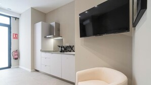 Une cuisine moderne avec des armoires blanches, une hotte de cuisinière en acier inoxydable et un téléviseur à écran plat fixé au mur.