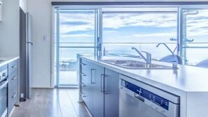 A modern kitchen with a large window, stainless steel appliances, and a view of the sky.