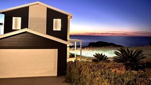 A modern two-story house with a garage, located near a beach with a view of the ocean and a clear night sky.