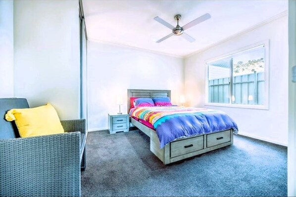 A bedroom with a bed, a nightstand, a chair, a ceiling fan, and a window.