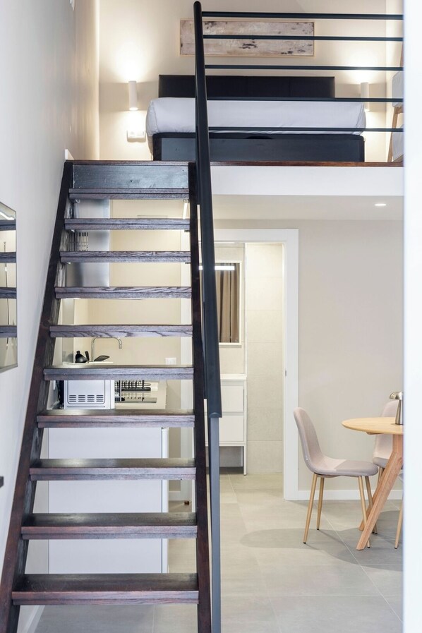Un intérieur moderne avec un escalier en bois, un coin repas comprenant une table et des chaises, et un espace cuisine équipé d’appareils électroménagers.