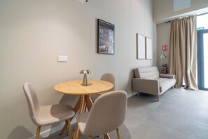 Un salon moderne avec une table ronde en bois, deux fauteuils beige, un canapé beige et un tableau abstrait encadré accroché au mur.