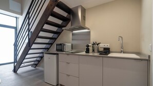 A modern kitchen with a built-in microwave, a coffee maker, and a sink. There is a small refrigerator and a staircase with a wooden railing. - VLC HOST - Sumsi J (Valencia)