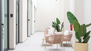 A corridor with wicker chairs and potted plants, leading to a door with a sign. - VLC HOST - Sumsi J (Valencia)