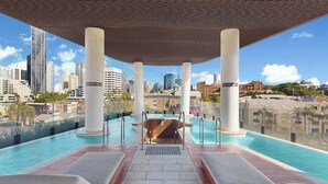 An infinity pool with lounge chairs, a view of the city skyline, and a covered area with columns. - Cosy Corner Fortitude Valley (Brisbane)