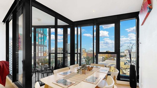 A modern dining area with a large table, chairs, and a view of the city through large windows. - Cosy Corner Fortitude Valley (Brisbane)