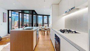 A modern kitchen with a central island, a dining area with chairs, and large windows offering a city view. - Cosy Corner Fortitude Valley (Brisbane)