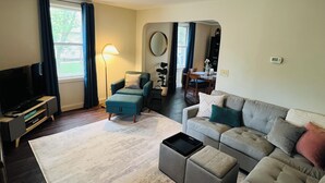 Ein Wohnzimmer mit einer Couch, einem Hocker und einem Fernseher auf einem Schrank.