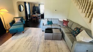 Ein Wohnzimmer mit grauem Sofa, blauem Sessel und einem Essbereich mit Tisch und Stühlen.