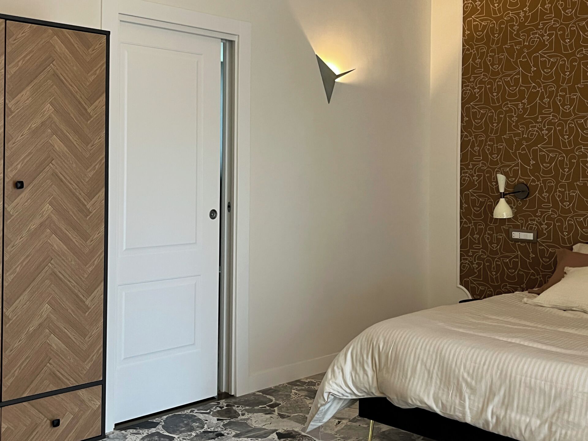 Une chambre à coucher comprenant un lit, une armoire, une porte et un luminaire fixé au mur.