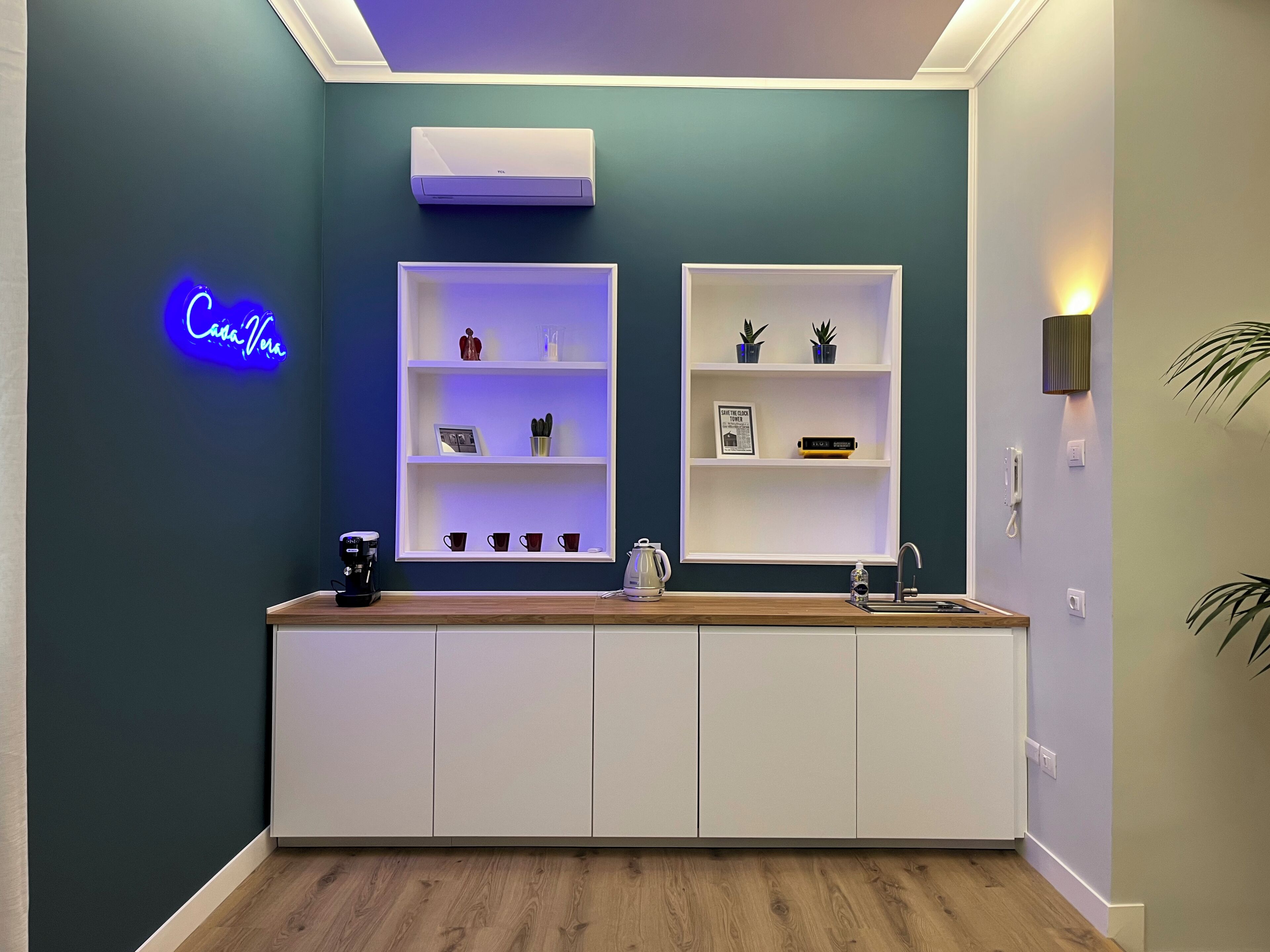 A modern kitchen with white cabinetry, a neon sign, and a built-in shelf unit.