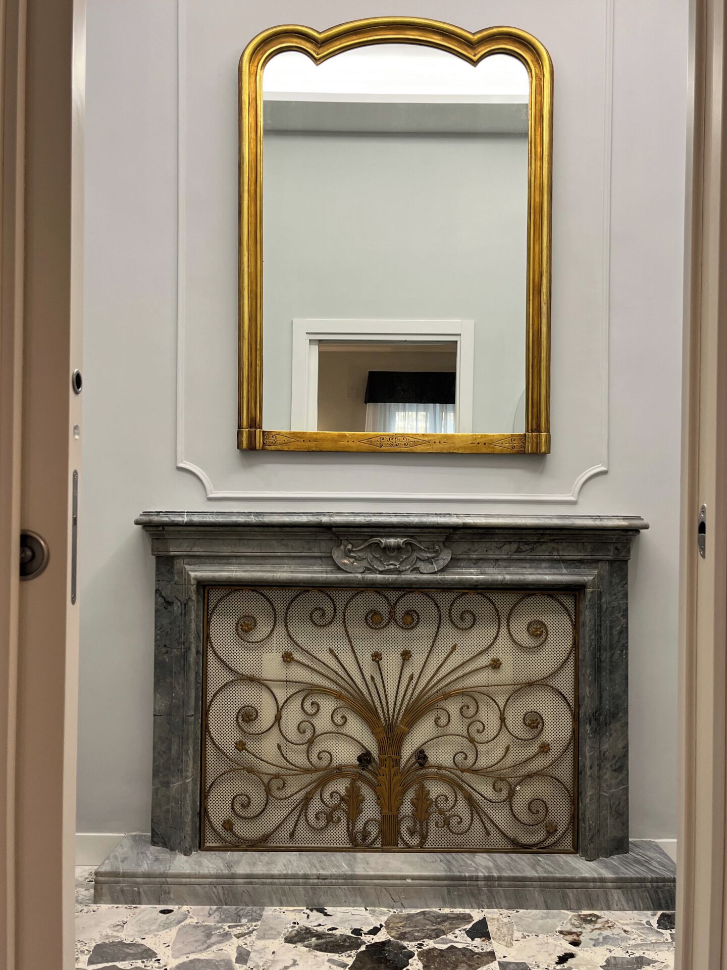 A marble fireplace with an ornate metal grate and a gold-framed mirror above it.