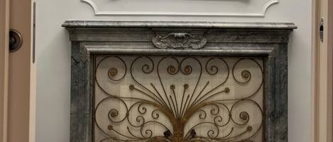 A marble fireplace with an ornate metal grate and a gold-framed mirror above it.