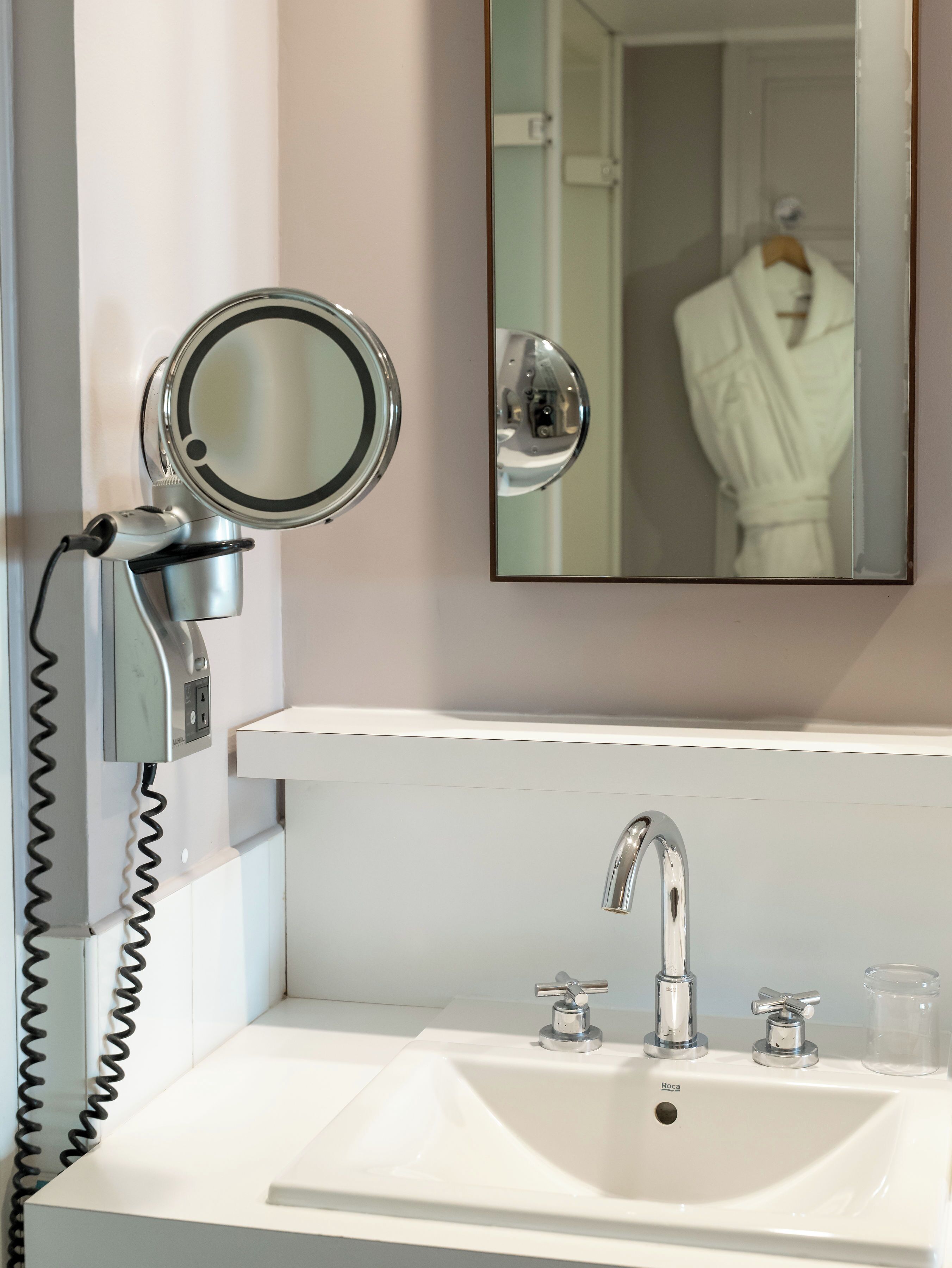 A bathroom with a white sink, a mirror, and a hairdryer mounted on the wall.