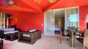 Una habitación con pared roja, ventilador de techo, muebles de mimbre y puerta corrediza de vidrio que da a otra habitación.