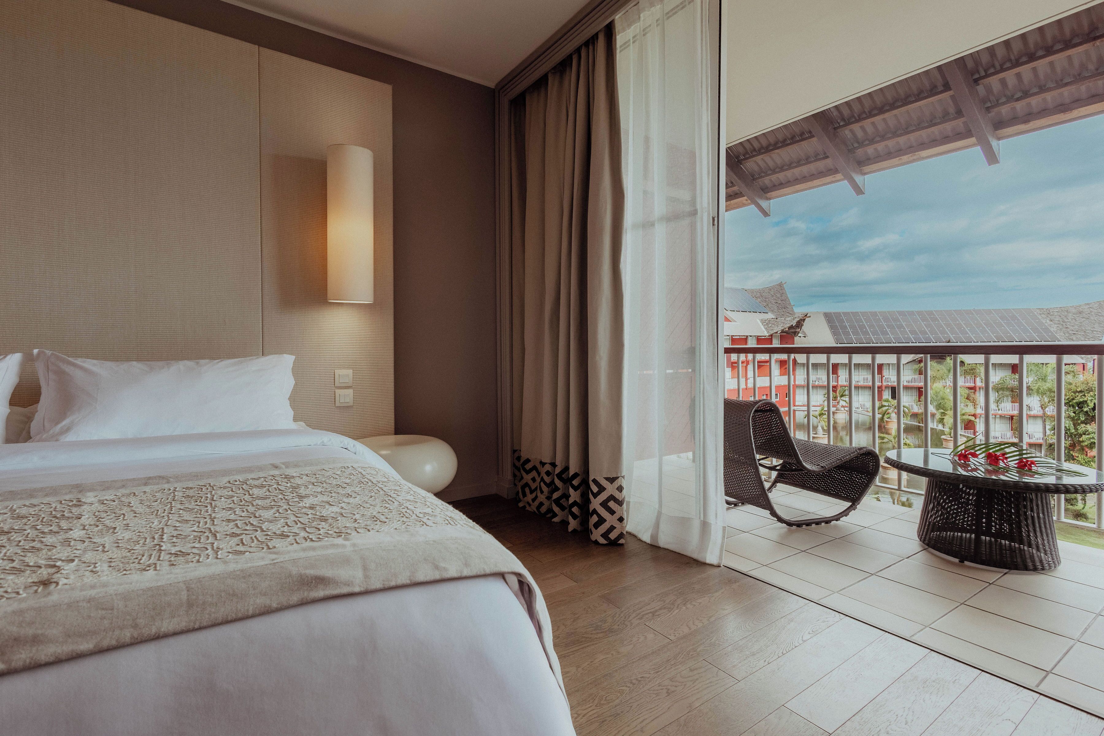 A hotel room with a bed, a round table, a chair, and a balcony with a view.