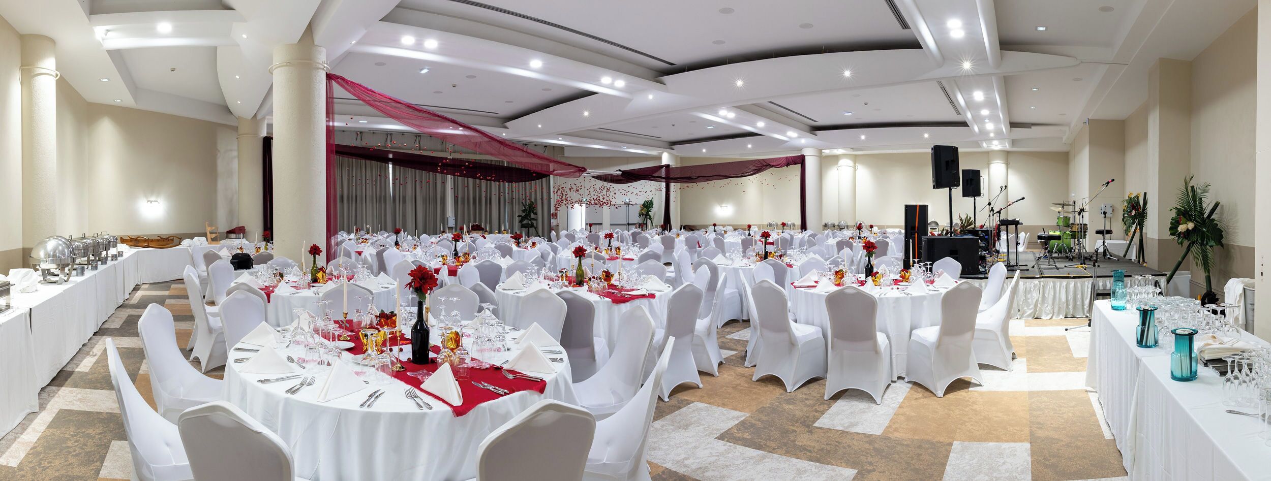 Un salón de banquetes con mesas redondas, sillas blancas y detalles en rojo.
