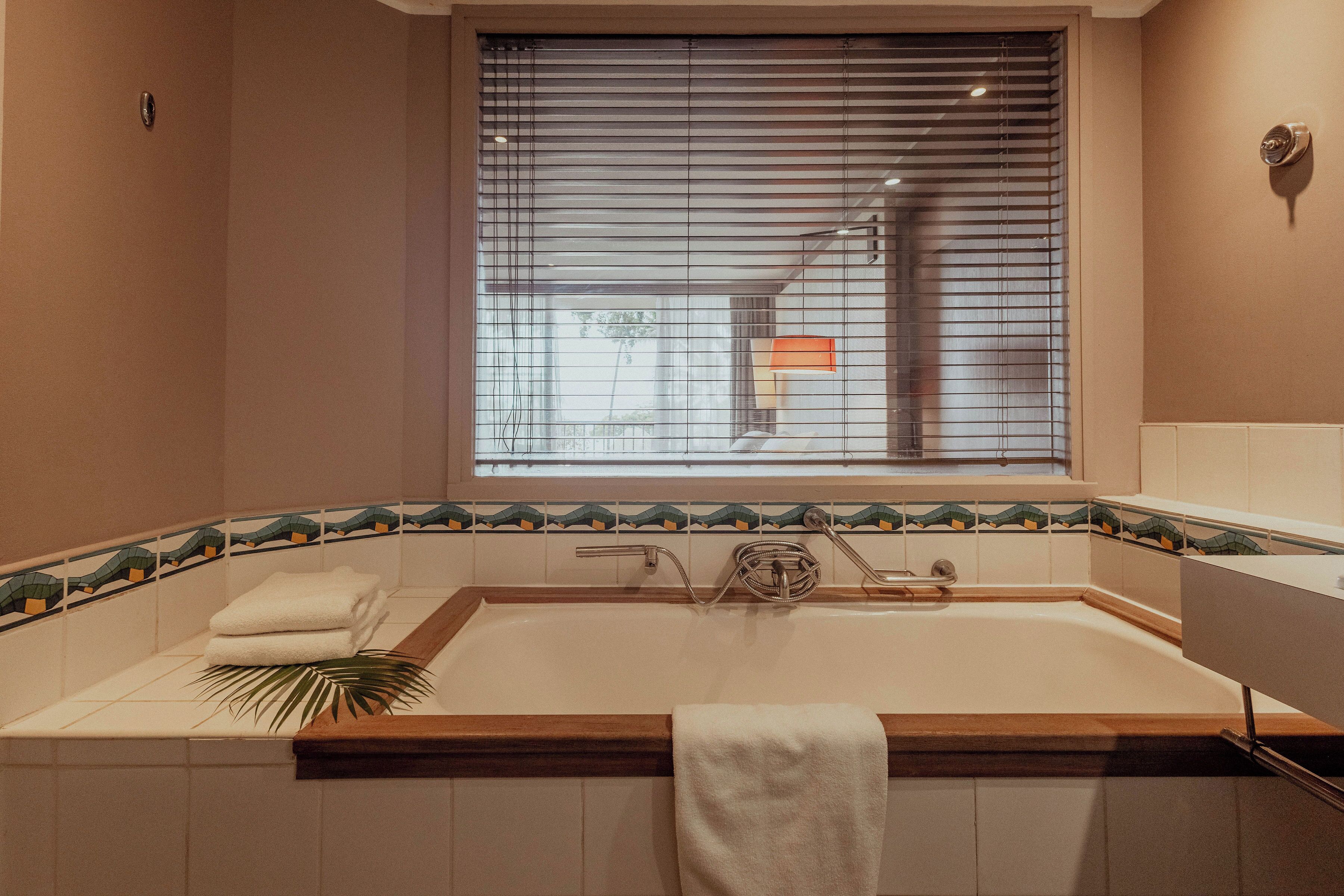 Une salle de bain avec une baignoire, une fenêtre avec des stores et un porte-serviettes.