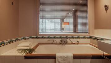 Une salle de bain avec une baignoire, une fenêtre avec des stores et un porte-serviettes.
