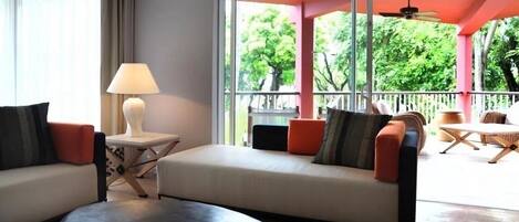 Una sala de estar moderna con un sofá, una mesita con una lámpara y vistas al exterior a través de amplios ventanales.