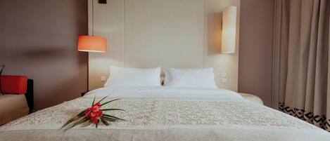 A hotel room with a bed, a nightstand, a lamp, and a window with curtains.