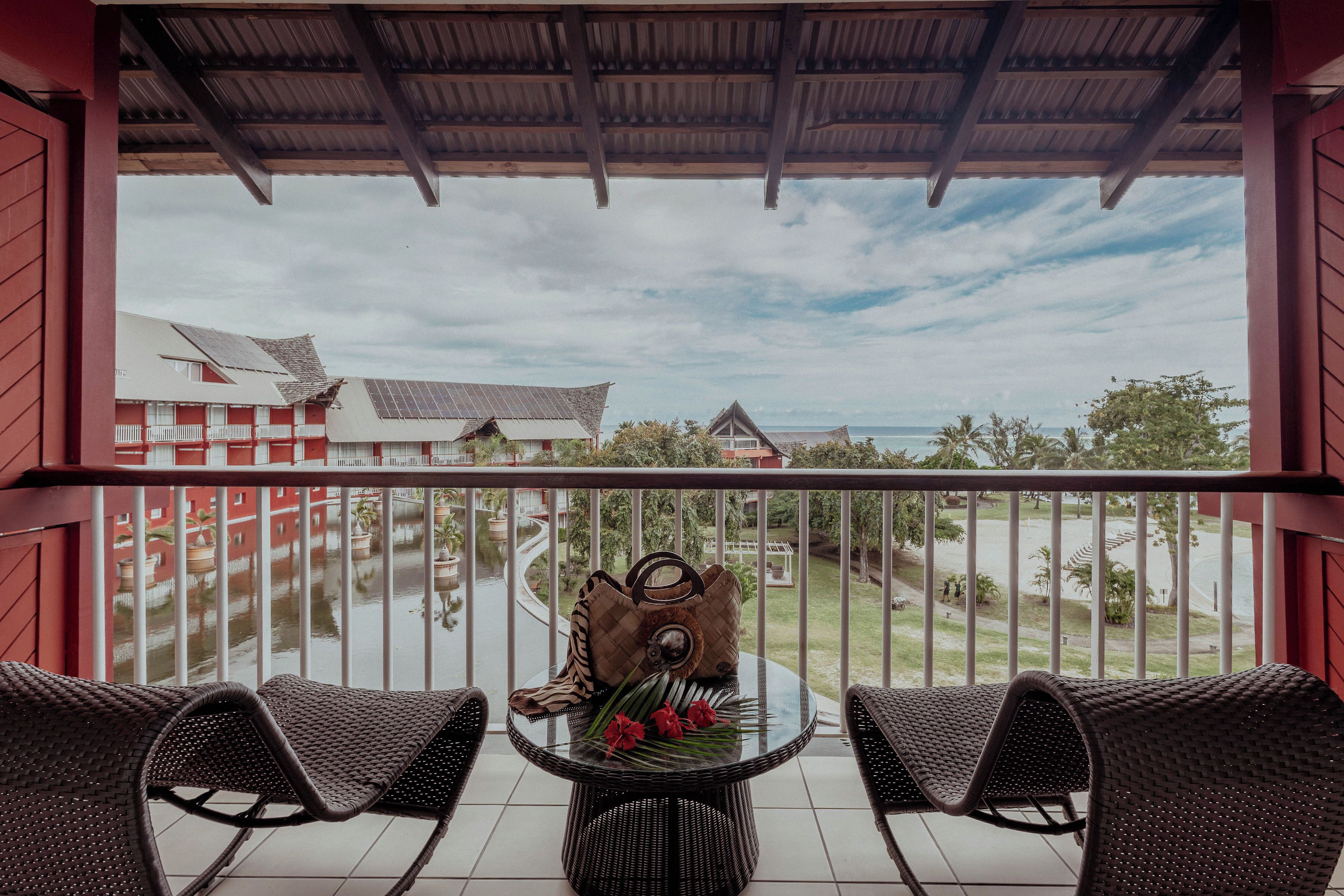 A balcony with wicker chairs, a glass table, and a view of a body of water and buildings.