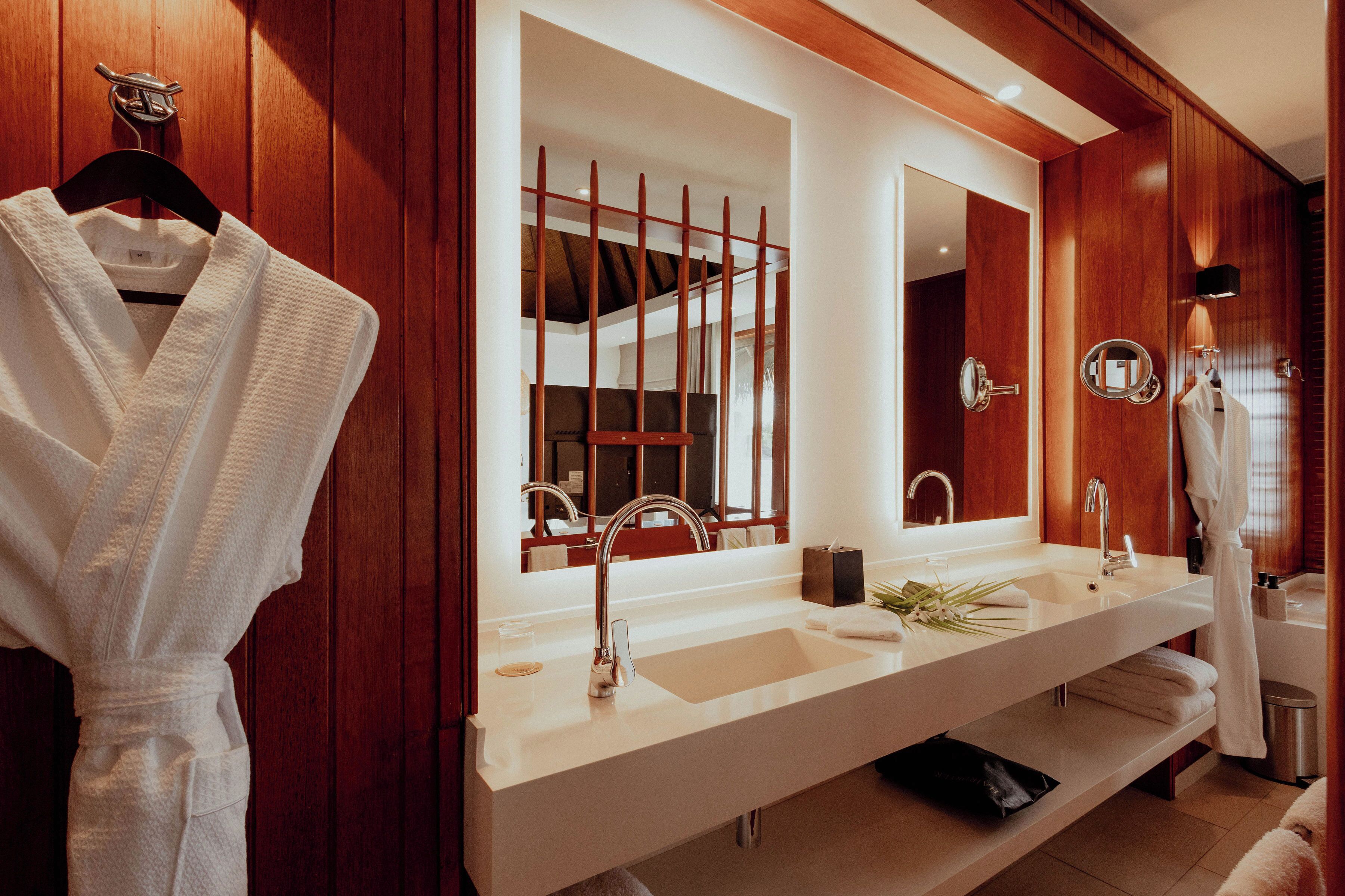 A modern bathroom with a wooden vanity, two sinks, a large mirror, and a towel rack.