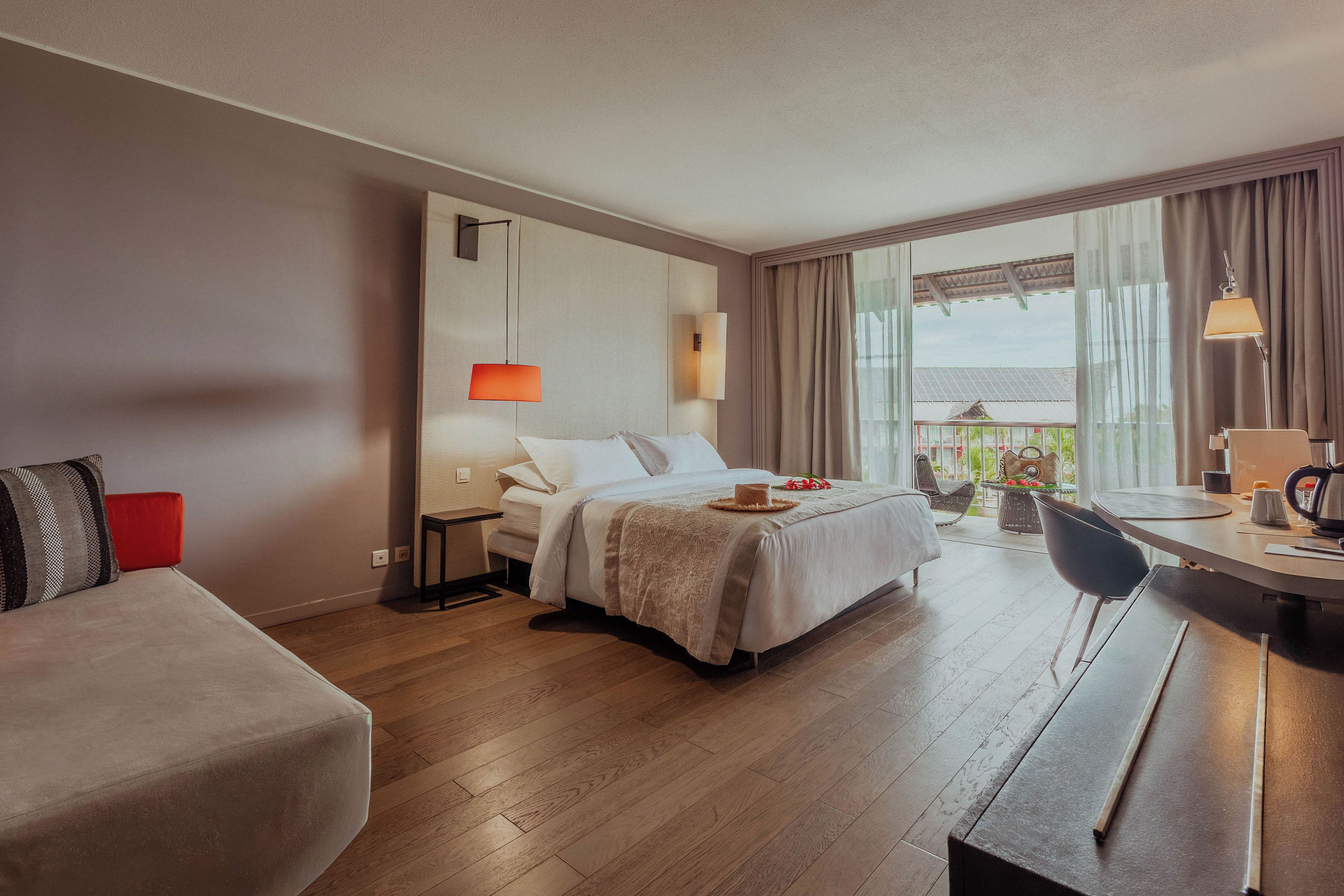 A hotel room with a bed, a desk, a chair, and a balcony with a view.