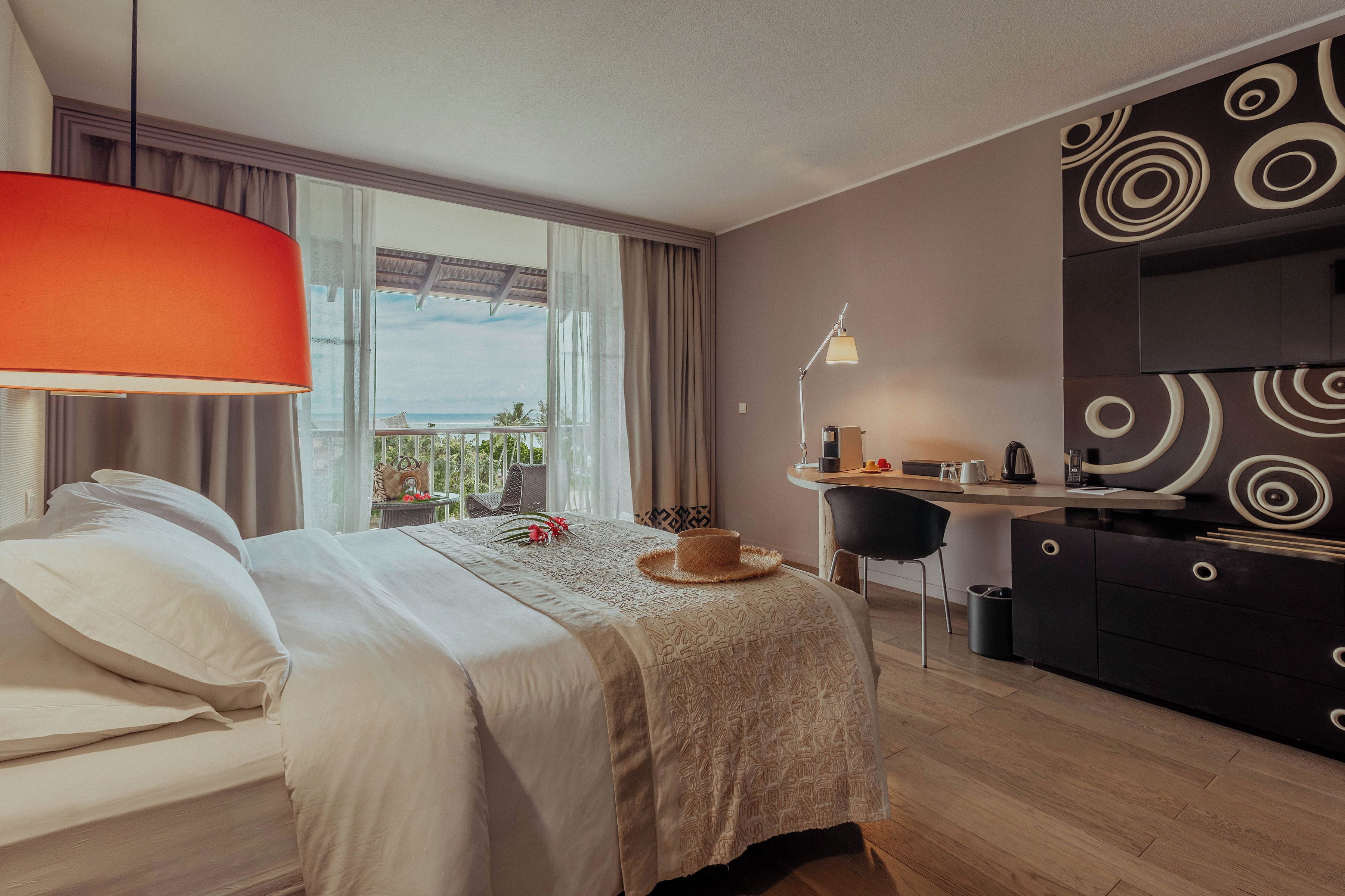 A hotel room with a bed, a desk, a chair, a lamp, and a view of the outdoors.