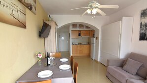 Ein Essbereich mit Tisch für vier Personen, einer Couch, einem Deckenventilator und einer Küche im Hintergrund.