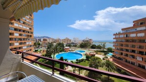 Ein Balkon mit Blick auf einen Poolkomplex, umgeben von Palmen und Wohnhäusern.