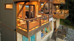 Una cabaña de madera de varios niveles, con balcones, ventanas amplias y zonas de estar al aire libre.