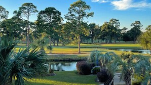 Un parcours de golf avec un étang, des arbres et un ciel bleu dégagé.