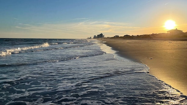 Une plage avec des vagues, un ciel dégagé et un soleil couchant.