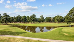 Un parcours de golf avec un étang, des arbres et un ciel dégagé.