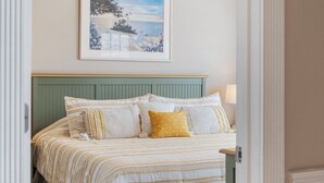 Un lit bien fait, avec une literie à rayures et deux oreillers, une tête de lit verte et un tableau encadré accroché au mur.