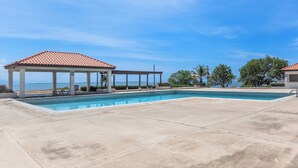 A swimming pool with a covered area and lounge chairs, surrounded by trees and a clear sky. - Stunning View, A Pool, Beach Access - Book Now! (Portmore)