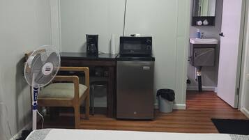 Ein kompakter Wohnbereich mit Küchenzeile, einem an der Wand befestigten Flachbildfernseher, einem kleinen Kühlschrank, einer Mikrowelle, einem Ventilator und einem Waschbecken.